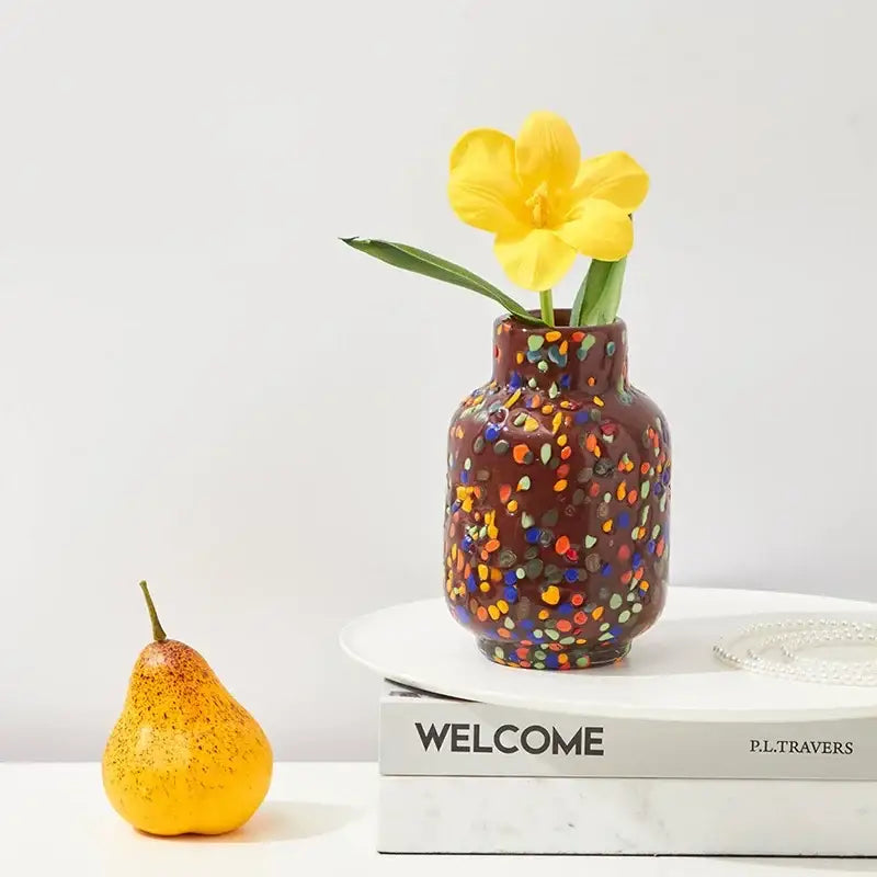 A brown ceramic decorbites glass vase with colorful speckles holds a single yellow tulip for home decor