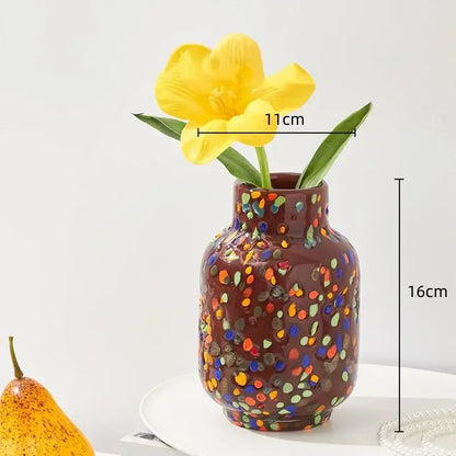 A brown ceramic decorbites glass vase with colorful speckled patterns holds a single yellow tulip for home decor