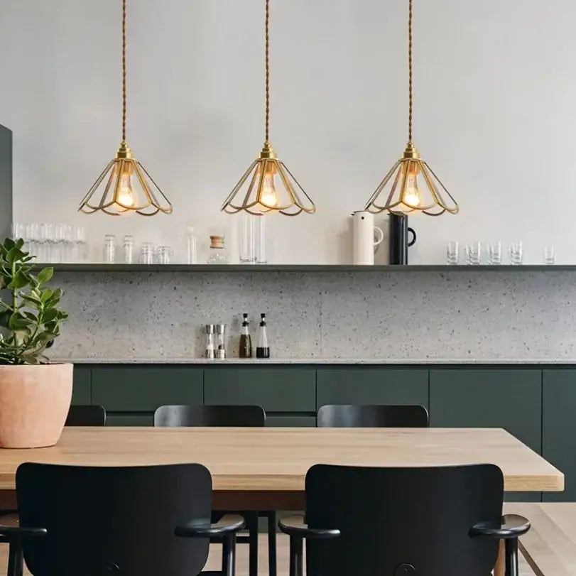 Three elegant brass decorbites glass vintage pendant lights with geometric wireframe shades hang above a dining table