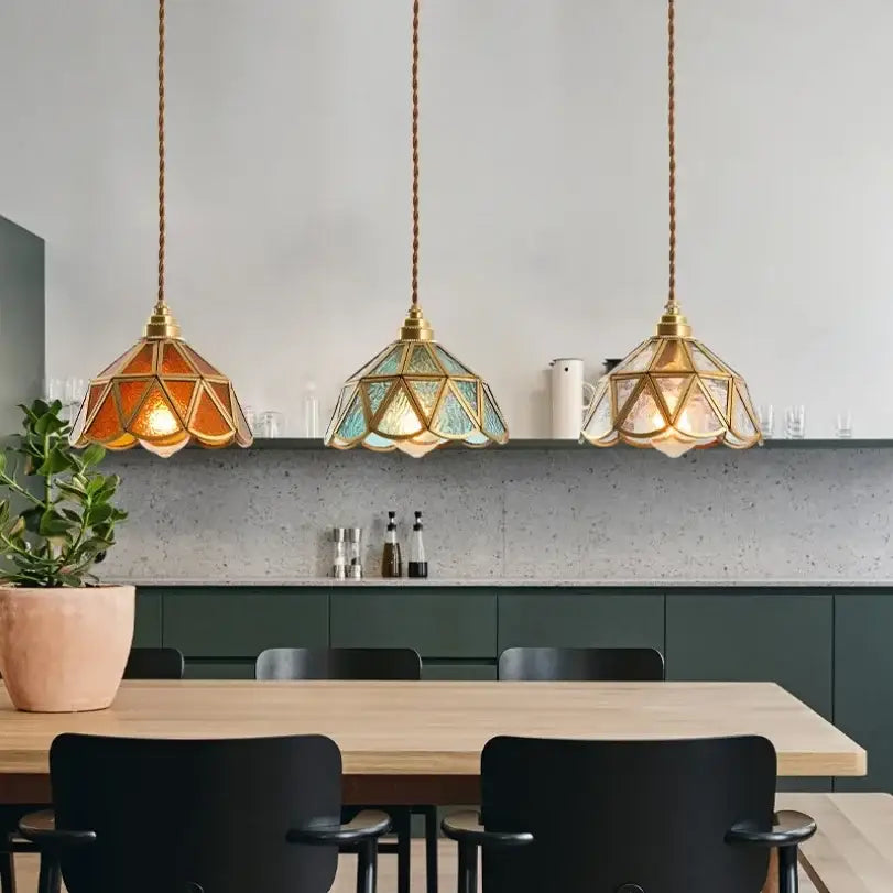 Three decorbites glass vintage pendant lights with amber and teal stained-glass shades hanging by twisted brass cords