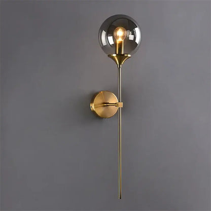 A sleek brass decorbites glass wall lamp with smoked glass globe and exposed filament bulb for bedroom lighting