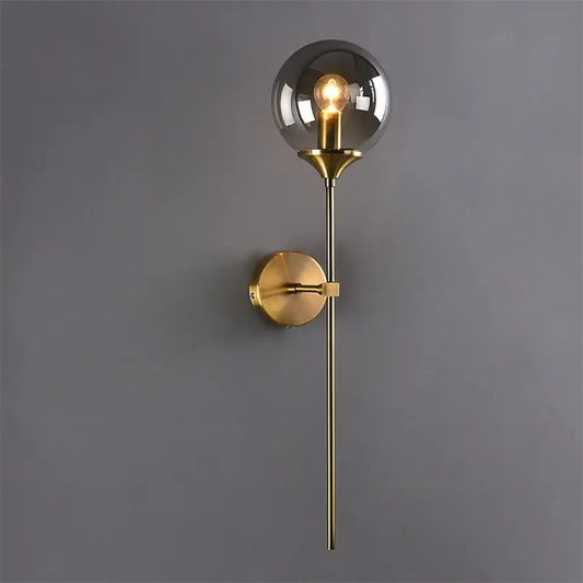A sleek brass decorbites glass wall lamp with smoked glass globe and exposed filament bulb for bedroom lighting