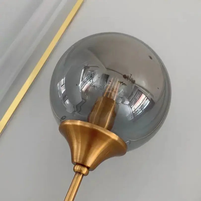 Decorbites glass wall lamp featuring a sleek smoked glass globe with a brass-finished base for bedroom lighting