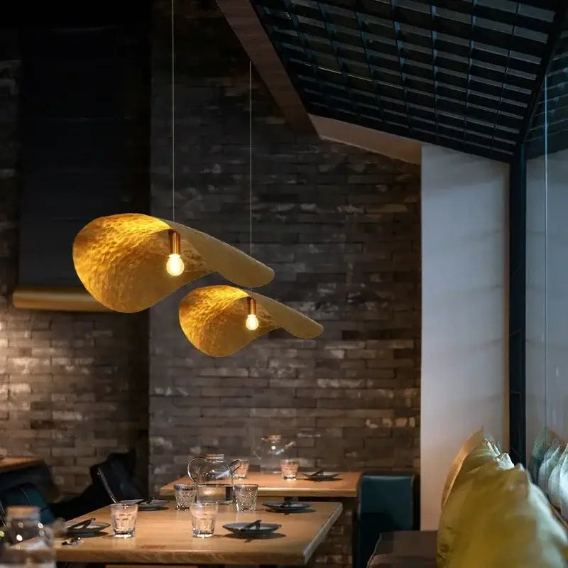 Two gold lotus leaf pendant lights in hammered metal with a leaf-like design hanging from the ceiling
