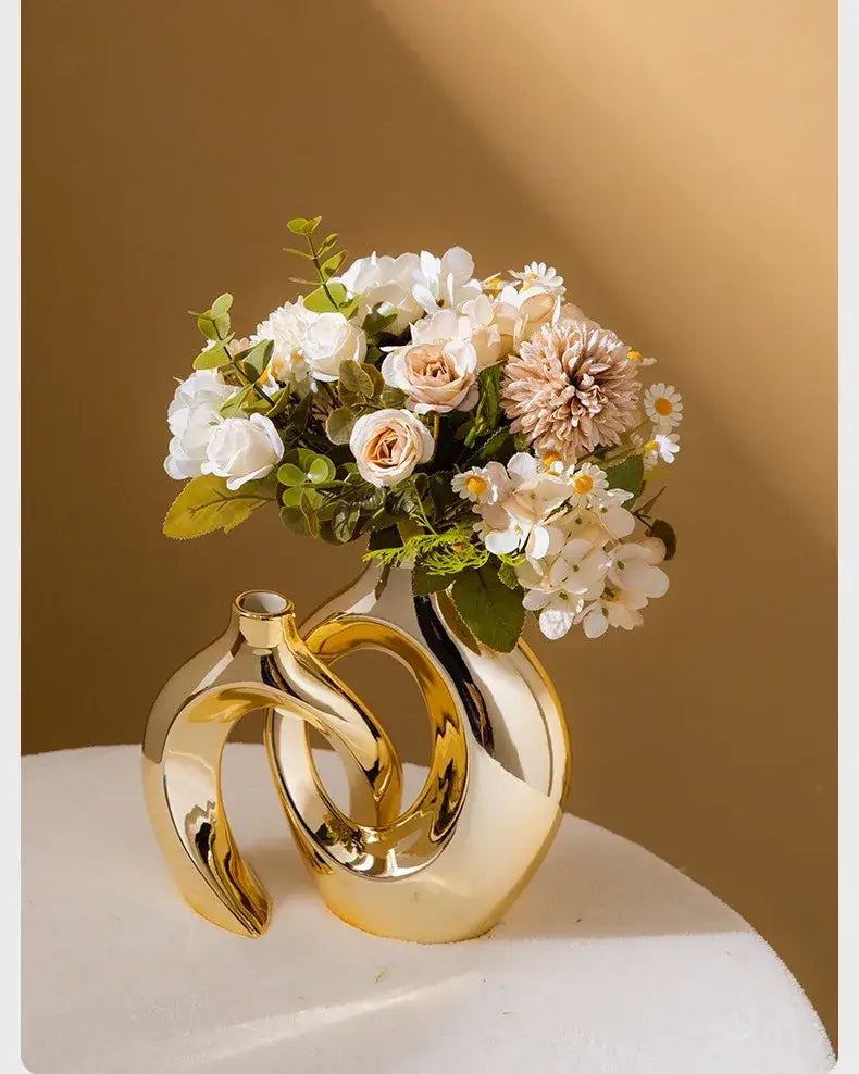 DecorBites golden flower vase with glossy ceramic finish and intertwined ring design holding white and blush flowers