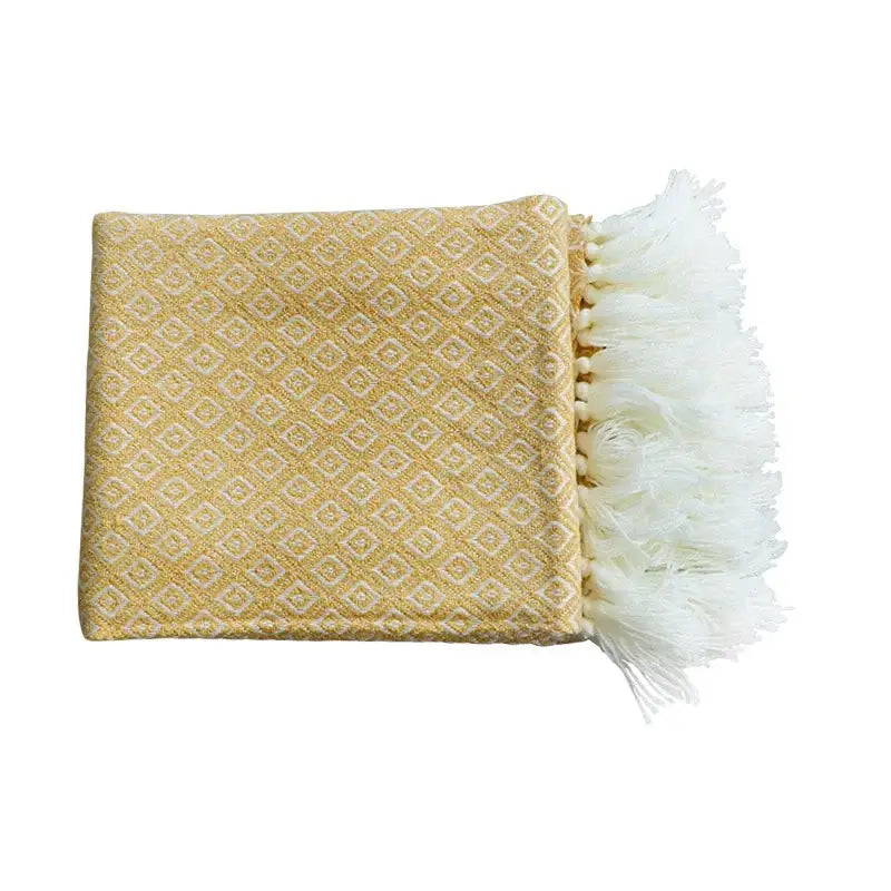 A soft yellow decorbites golden knitted blanket with cream geometric pattern and white fringe for living room use