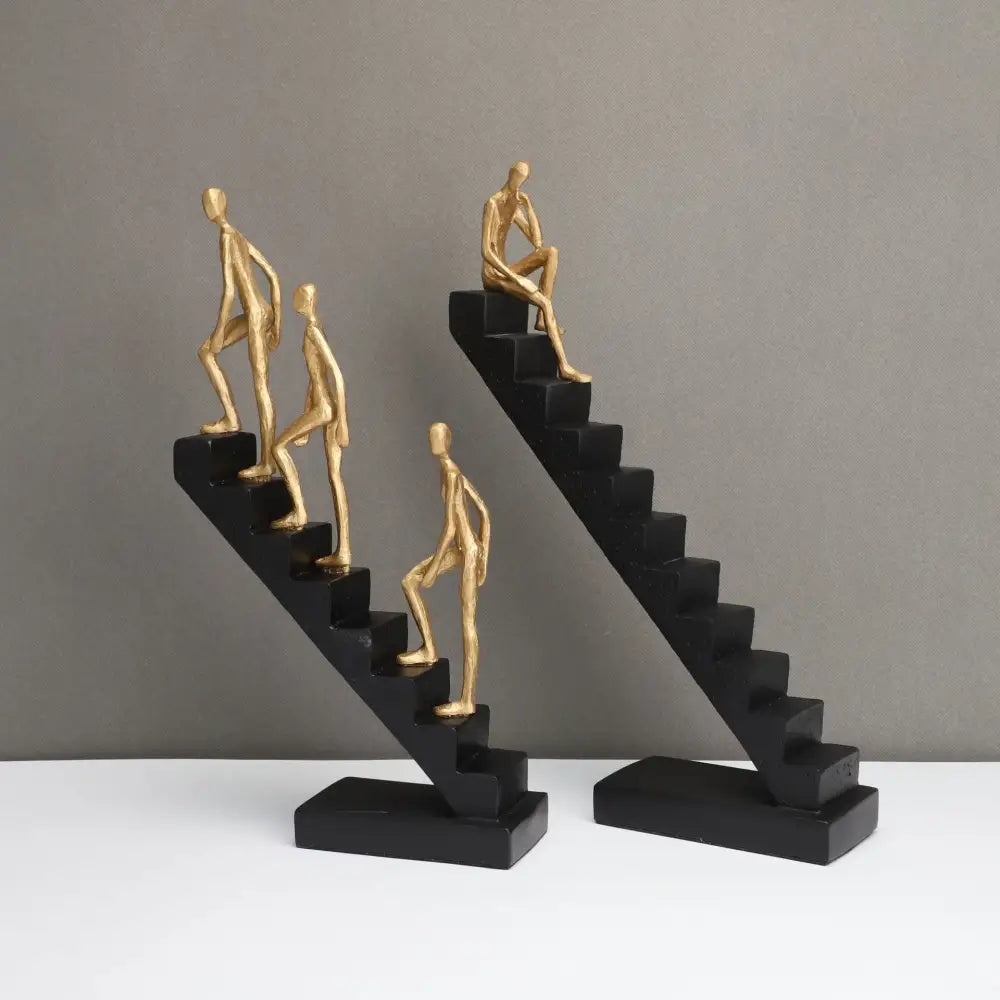 Two black staircase sculptures with golden humanoid figures in ascending and seated poses decorbites golden man climber decor