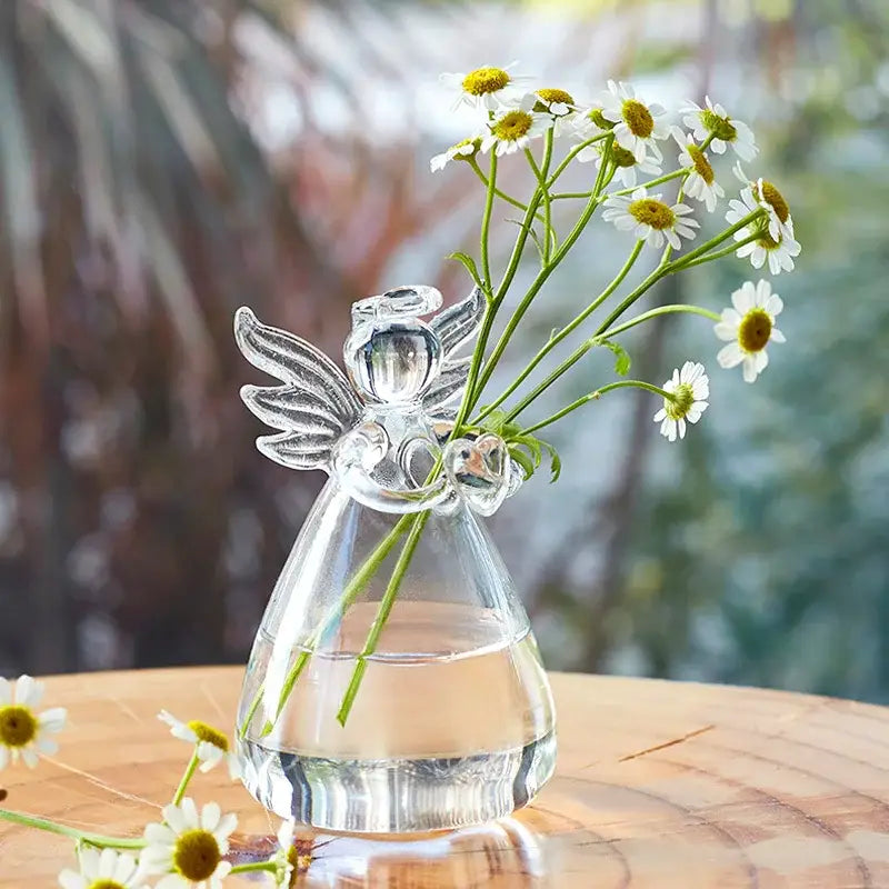 Clear glass angel shaped vase by DecorBites™ holding white daisies with yellow centers for home decor