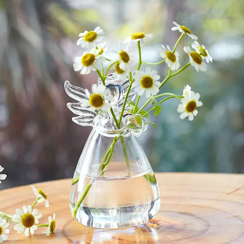 Clear glass handmade angel-shaped vase by DecorBites holding white daisies with yellow centers for home decor