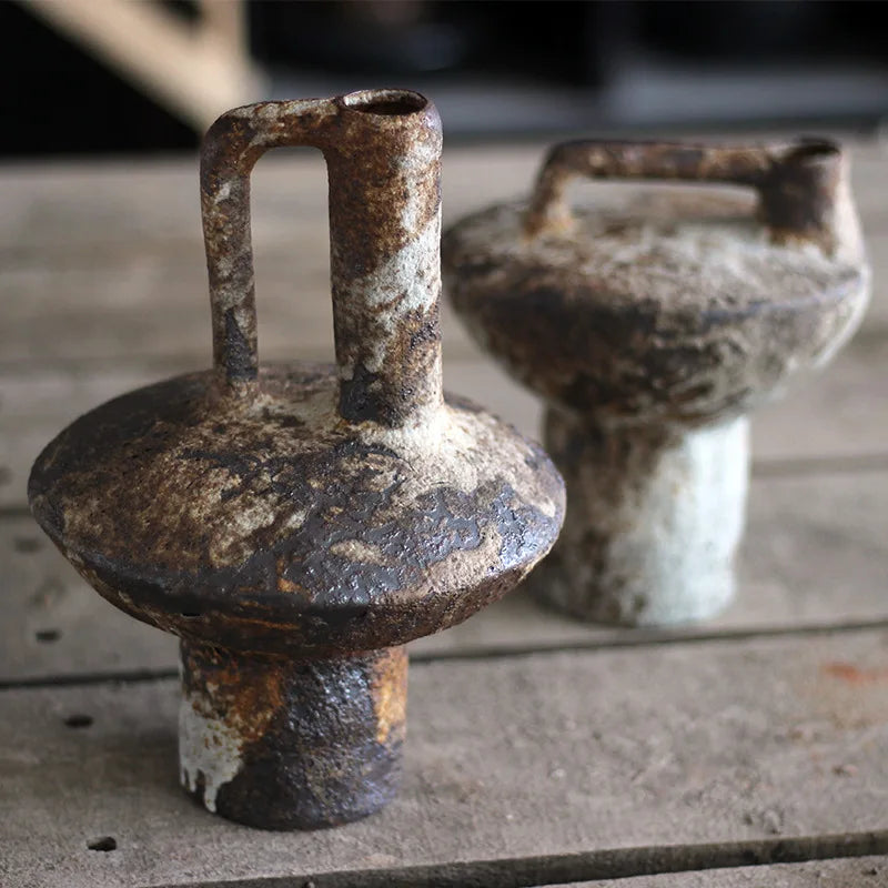 Rusty weathered iron weights with handle and rounded top next to a pottery vase for dried flowers by decorbites