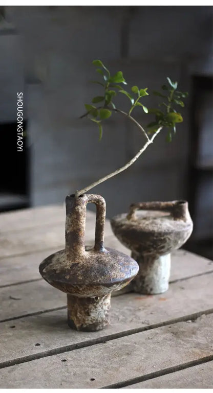 Rustic brown ceramic vase with handle and textured surface holding a green branch for dried flowers by decorbites