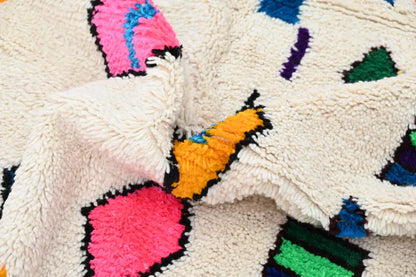Cream-colored handmade moroccan azilal rug with plush fibers and vibrant pink orange green blue and purple geometric patterns
