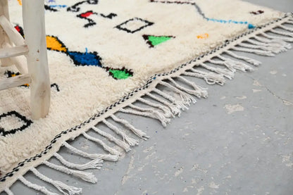 Cream-colored handmade moroccan azilal rug with colorful geometric patterns and white fringe 222 x 139 cm