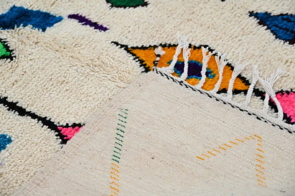 Cream-colored handmade moroccan azilal rug with vibrant geometric patterns and textured woolen surface by DecorBites™