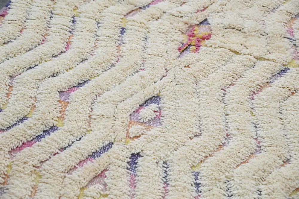 Cream-colored handmade moroccan azilal rug with textured zigzag woolen pattern and subtle pink purple yellow accents
