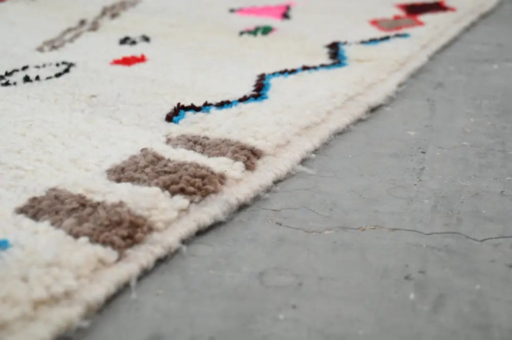 Cream-colored natural wool moroccan handmade azilal rug with textured geometric patterns in black blue pink and brown