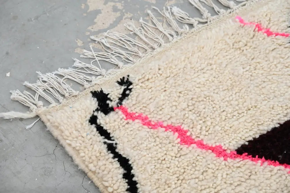 Cream-colored moroccan handmade azilal rug with black and pink geometric stripes and fringed edge by decorbites