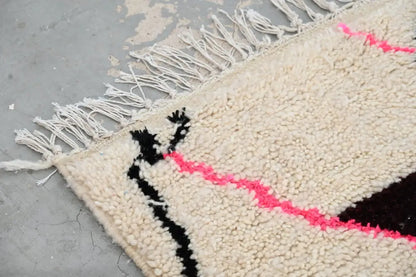 Cream-colored moroccan handmade azilal rug with black and pink geometric stripes and fringed edge by decorbites