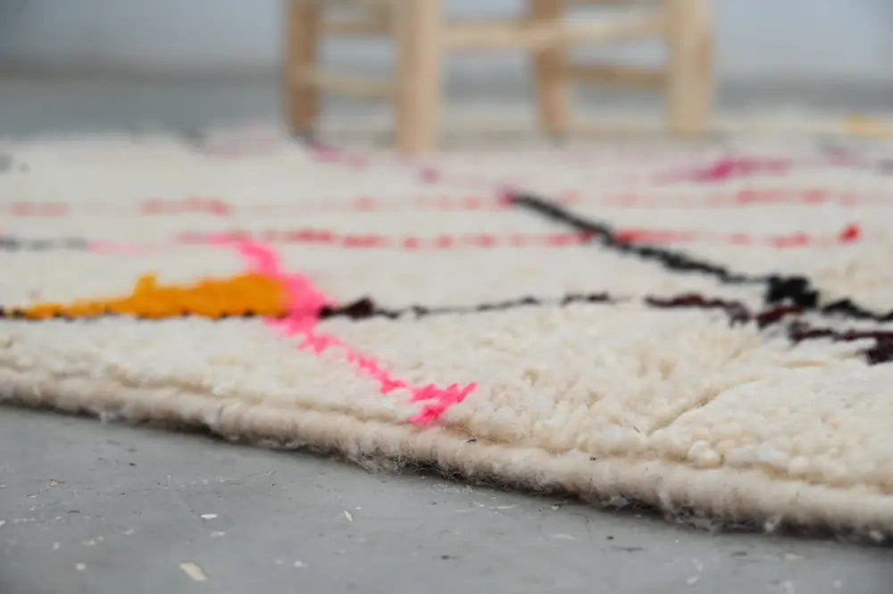 A cream-colored moroccan handmade azilal rug with bold black pink and orange geometric patterns showcasing moroccan craftsmanship
