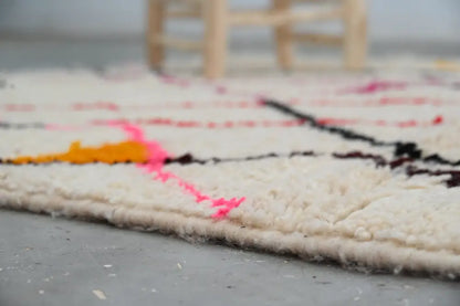 A cream-colored moroccan handmade azilal rug with bold black pink and orange geometric patterns showcasing moroccan craftsmanship