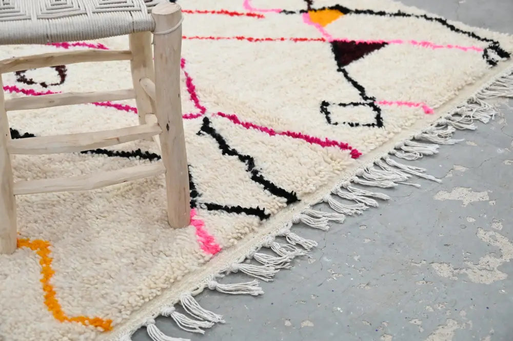 A cream-colored decorbites™ handmade moroccan azilal rug with bold geometric patterns and fringed edge