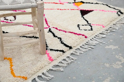 A cream-colored decorbites™ handmade moroccan azilal rug with bold geometric patterns and fringed edge