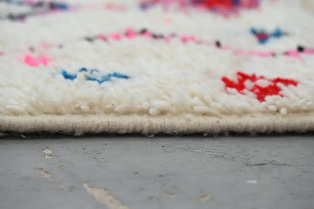 A cream-colored handmade traditional azilal rug with vibrant pink blue and red geometric patterns by DecorBites™