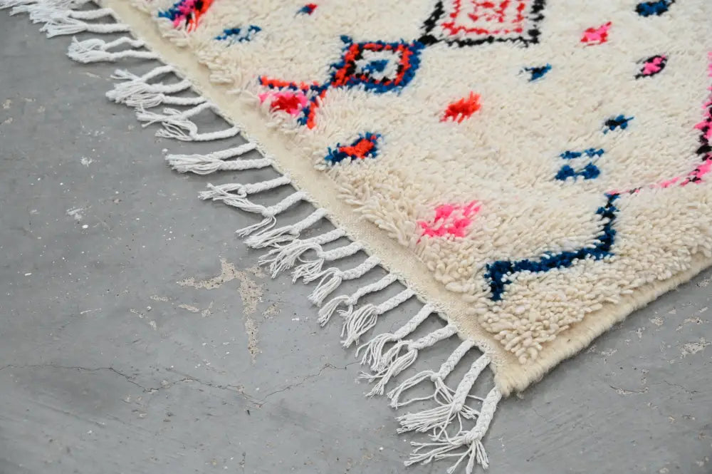 Cream-colored handmade traditional azilal rug with vibrant pink blue black geometric patterns and long white fringe