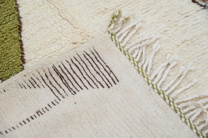 Cream-colored moroccan handmade azilal rug with textured wool surface, dark brown geometric stripes, and white fringes with green stitching