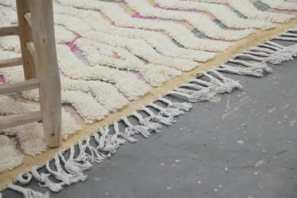 Cream-colored chunky-knitted handmade moroccan azilal rug with pink gray zigzag pattern and long white fringe 238x144cm