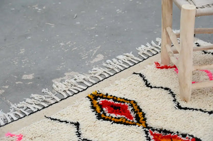 Cream-colored decorbites™ handmade azilal rug 240x150cm with bold red black orange geometric patterns and natural wool fringe