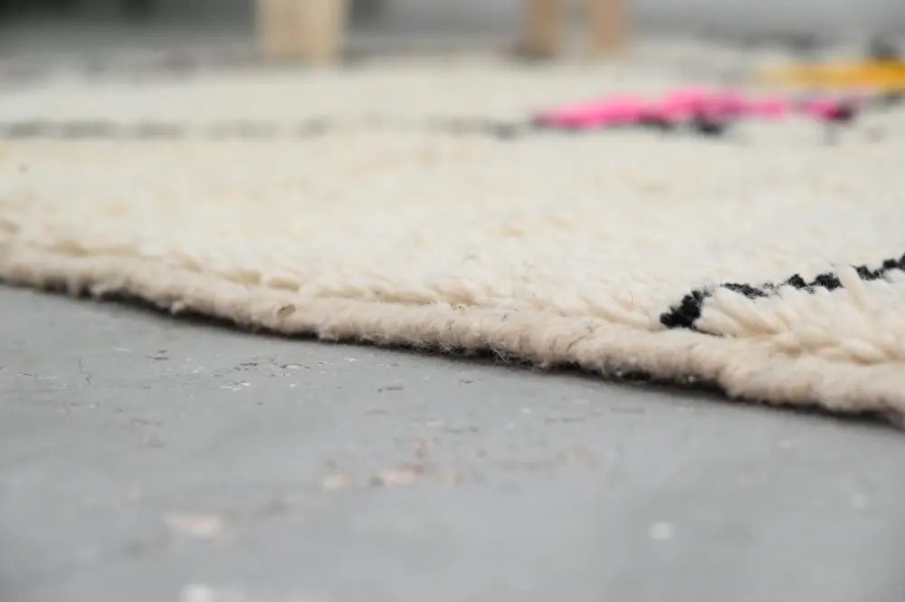 Cream-colored thickly woven wool moroccan azilal rug with textured fringe and bold black geometric patterns 240x152 cm