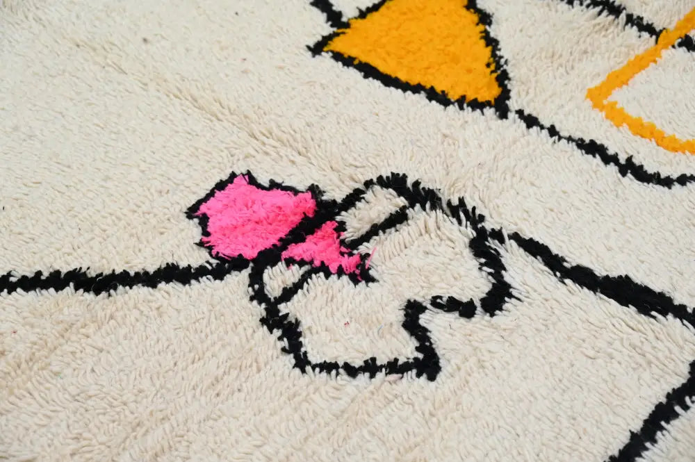 A cream-colored plush moroccan azilal rug with bold black outlines and vibrant pink and orange geometric shapes 240x152 cm