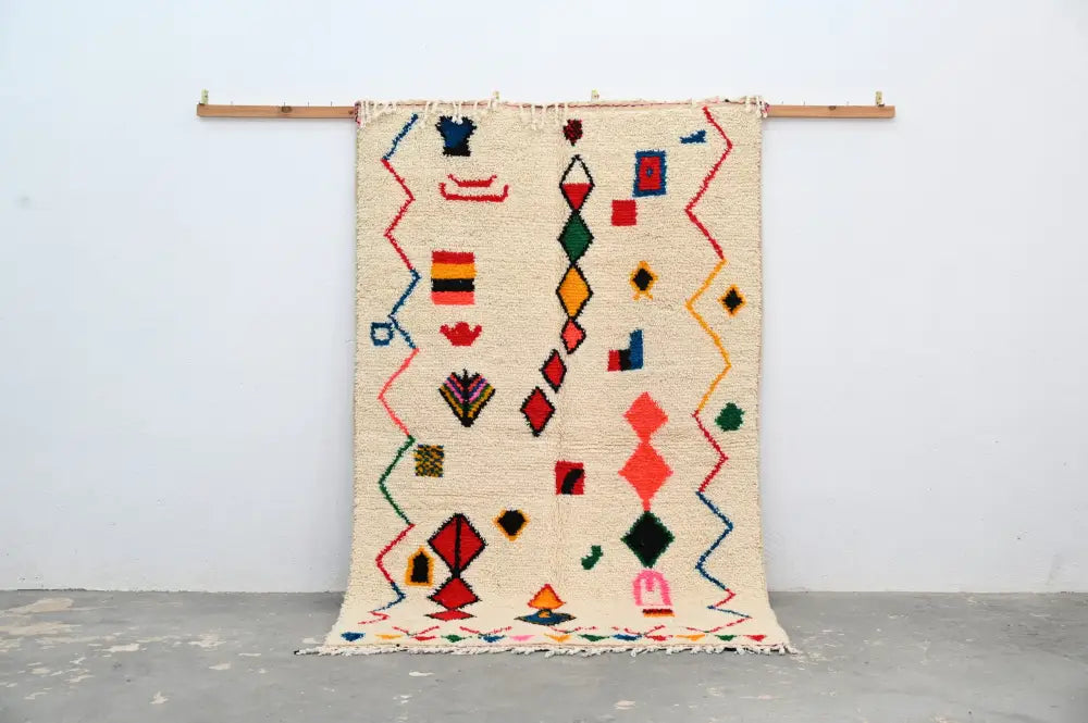 Beige handmade traditional azilal rug with colorful geometric patterns in red blue green and yellow on woolen surface