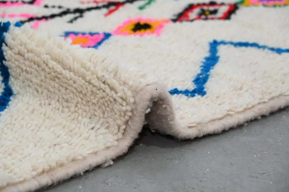 A plush handmade moroccan azilal rug in off-white with vibrant blue pink black and yellow geometric patterns