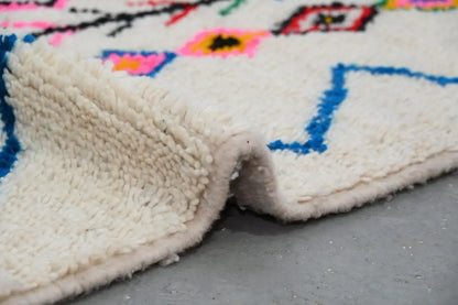 A plush handmade moroccan azilal rug in off-white with vibrant blue pink black and yellow geometric patterns