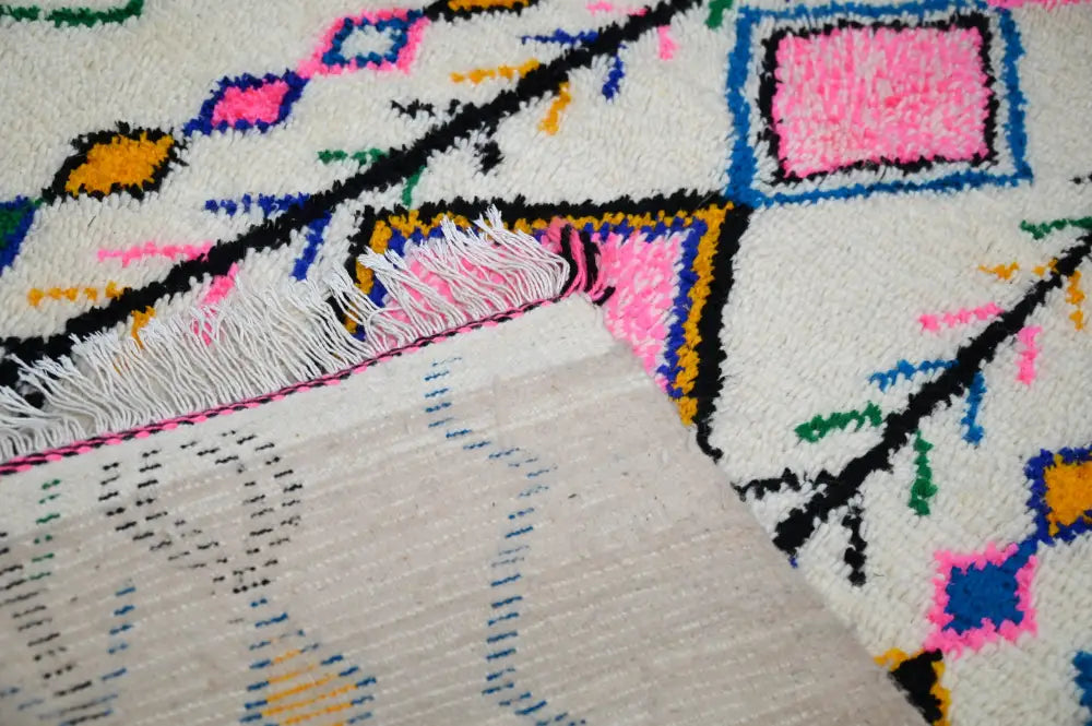 A vibrant handmade moroccan azilal rug with white base and bold pink blue yellow green and black geometric patterns