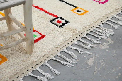 Cream-colored handmade Moroccan Azilal rug with bold red black yellow and pink geometric patterns and fringed edge