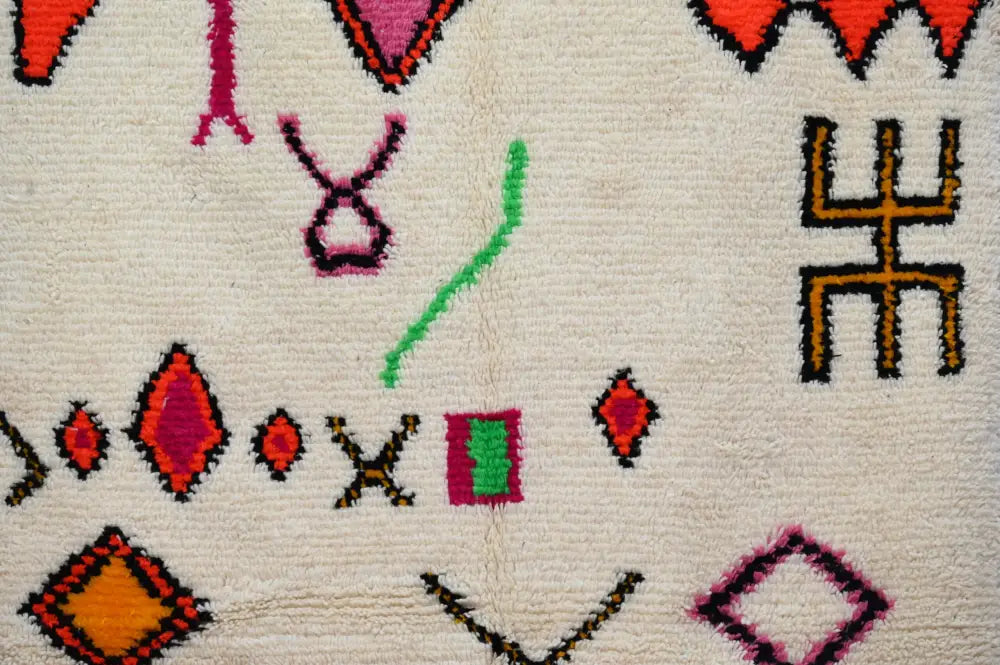 Cream-colored handmade moroccan azilal rug with vibrant red pink green and orange geometric patterns by decorbites