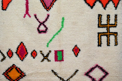 Cream-colored handmade moroccan azilal rug with vibrant red pink green and orange geometric patterns by decorbites