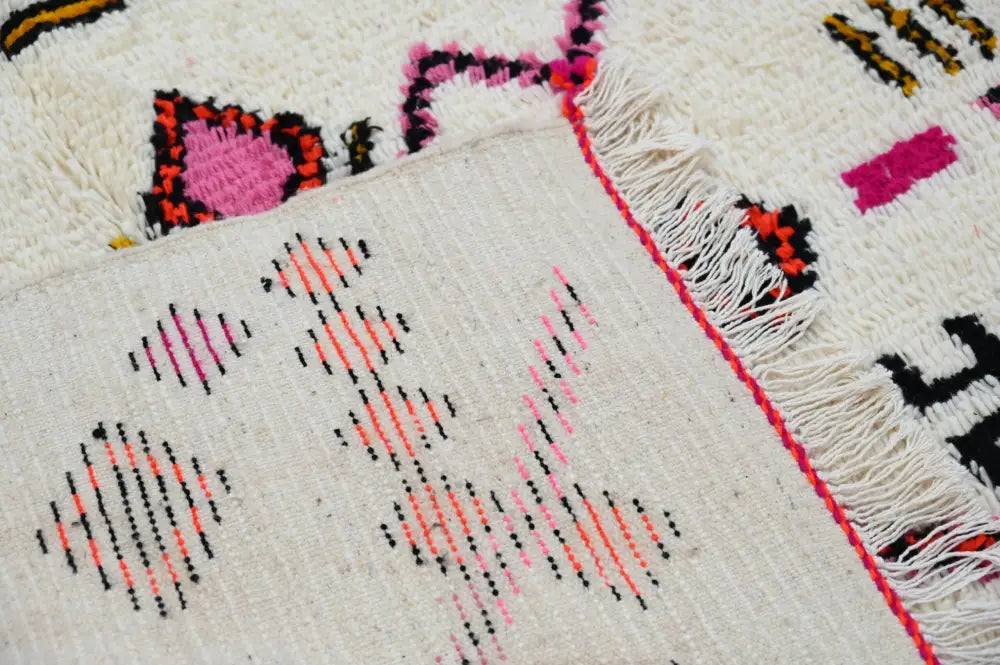 Cream-colored handmade moroccan azilal rug with pink black and orange geometric patterns and fringed edge 247x146 cm