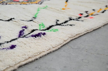 Cream-colored DecorBites™ handmade moroccan azilal rug with intricate black purple green and orange embroidered patterns