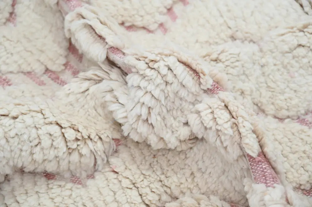 Cream-colored sherpa fabric with soft texture and subtle pink geometric patterns on handmade traditional azilal rug