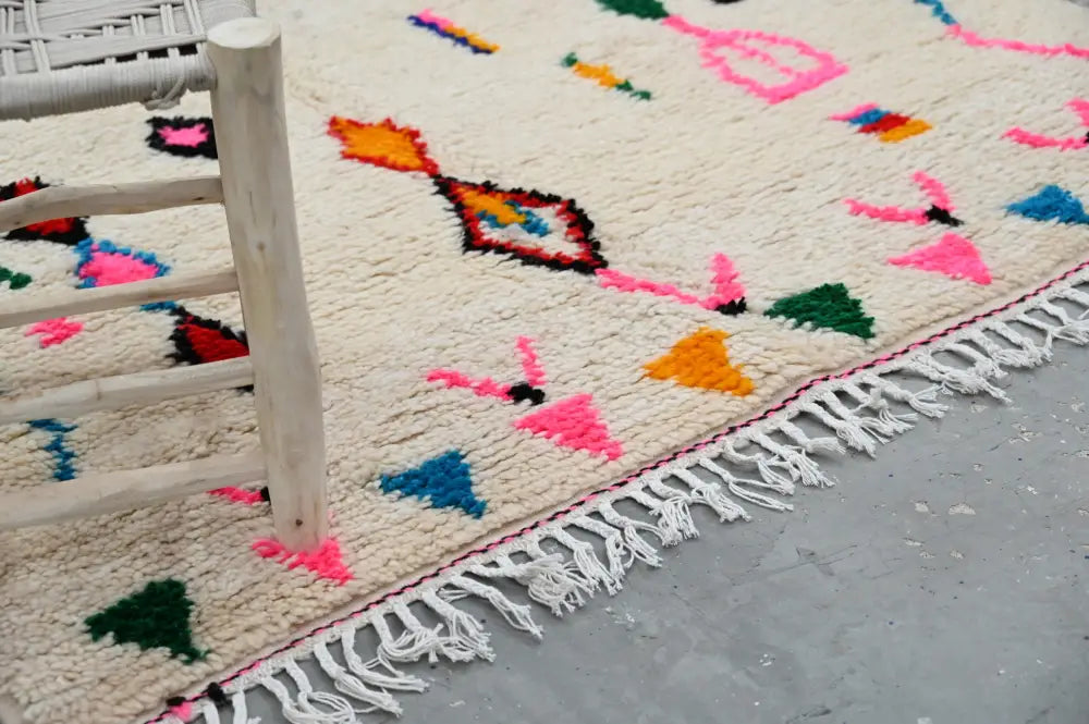 Cream-colored moroccan azilal rug with vibrant pink orange blue green geometric patterns and fringed edge by decorbites