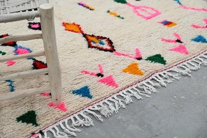 Cream-colored moroccan azilal rug with vibrant pink orange blue green geometric patterns and fringed edge by decorbites