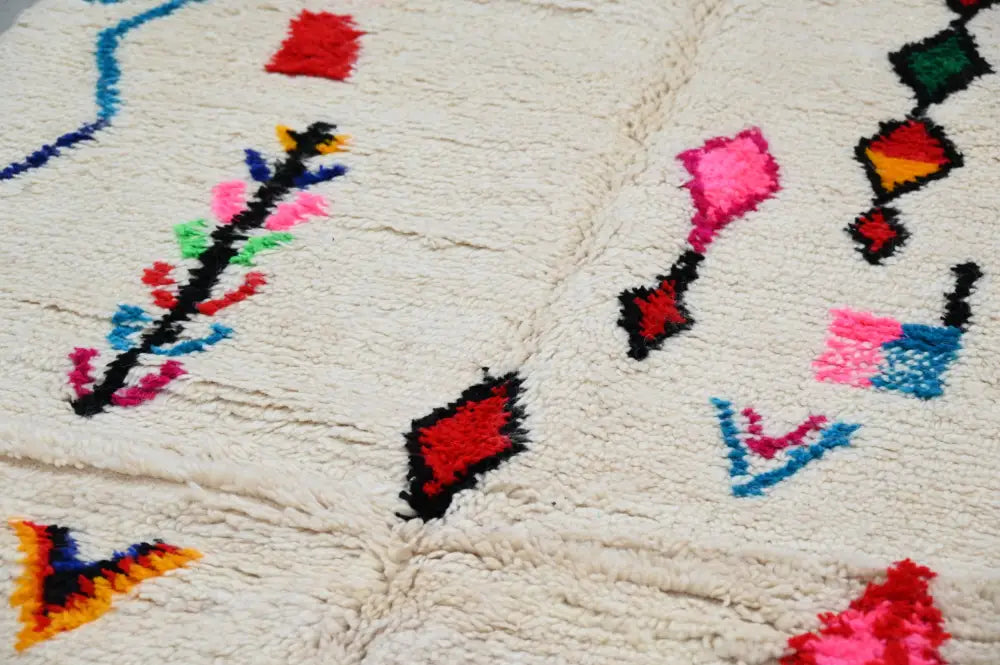 Cream-colored moroccan azilal rug by decorbites with fluffy texture and vibrant red pink blue green and black patterns