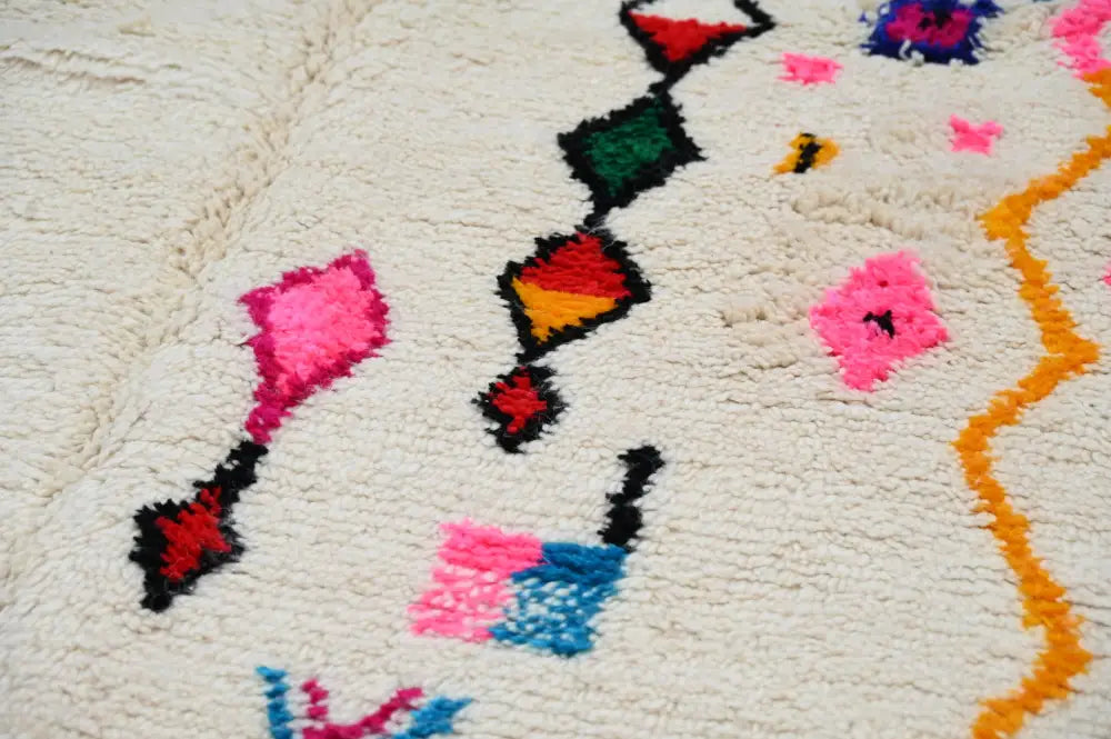 A plush off-white handmade moroccan azilal rug with vibrant geometric patterns in pink red green blue and orange 250x145 cm