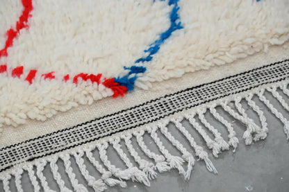 Cream-colored wool moroccan azilal rug with bold red and blue geometric patterns and white fringe 250x154cm