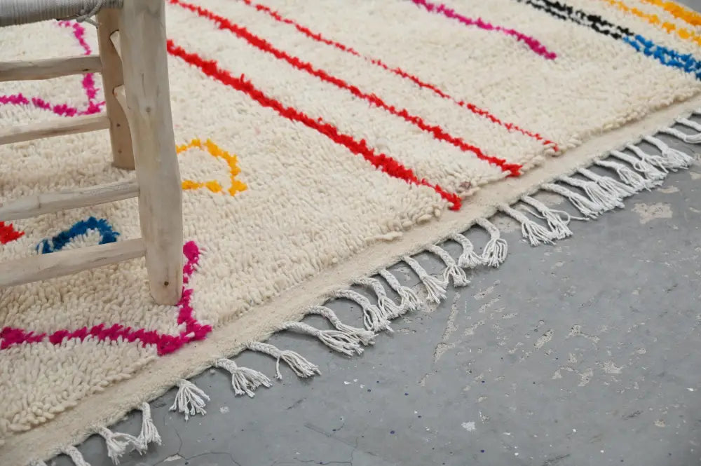 Cream-colored handmade traditional azilal rug with bold red pink yellow and blue geometric stripes and white tassels