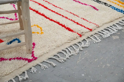 Cream-colored handmade traditional azilal rug with bold red pink yellow and blue geometric stripes and white tassels